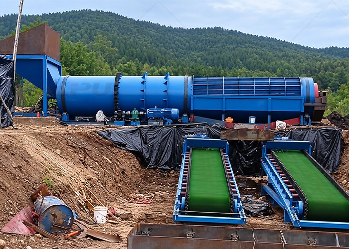 Rotary scrubber washing ore at an outdoor mineral processing site, with conveyors feeding and discharging material.