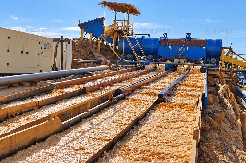 Portable gold sluice channels processing water and gold-bearing material at an alluvial mining site.